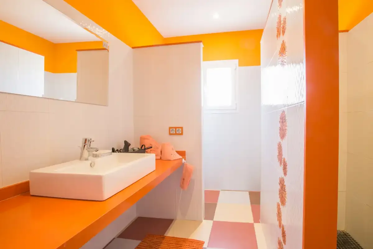 A bright bathroom with an orange counter and a white vessel sink.