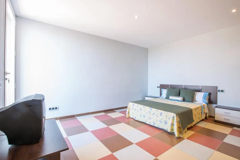 A bedroom with a bed, patterned bedding, and colorful square floor tiles.