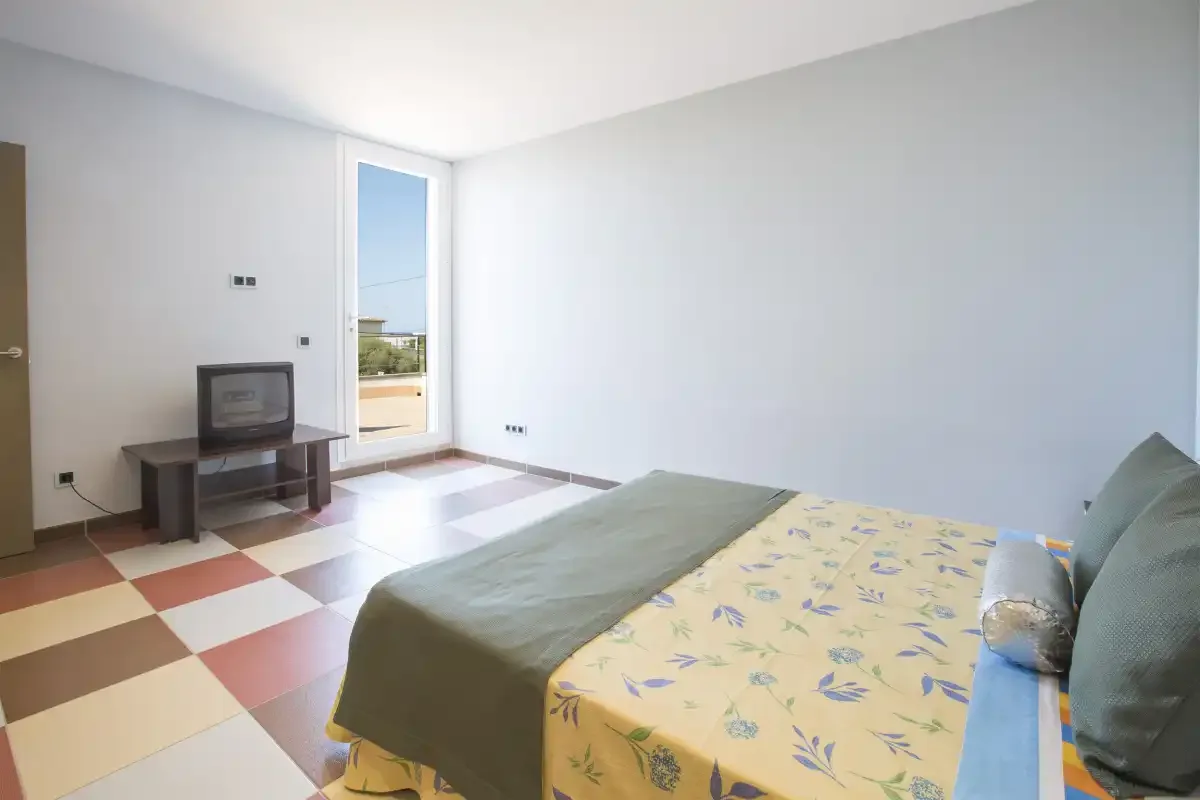 A bedroom with a bed, a small television, and a glass door to the outside.