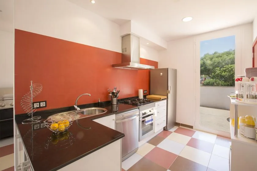 A modern kitchen with a red backsplash, dark countertop, and built-in appliances.