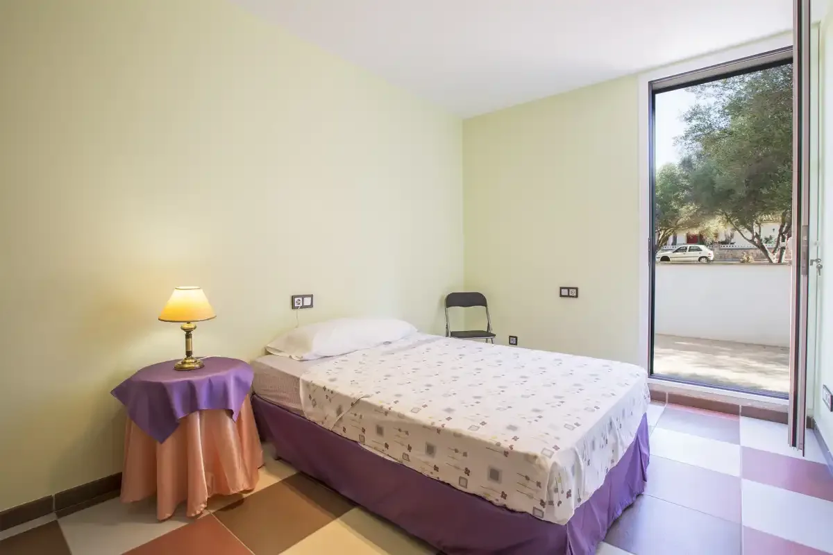 A bedroom with a bed beside a small table and an open glass door.