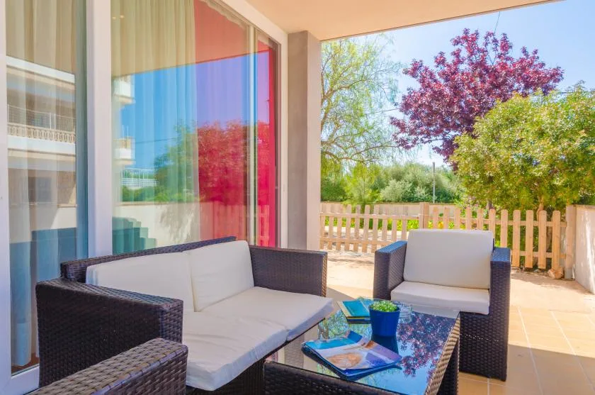 A patio seating area with dark wicker furniture and a glass table overlooks a fenced garden.