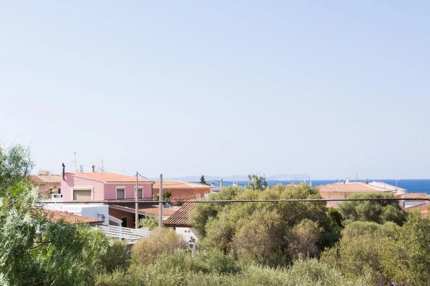 A coastal residential scene with tiled rooftops and trees beneath a clear sky.