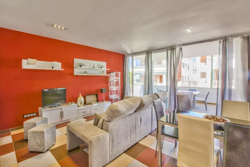 A living room with seating, a television, and large windows opening onto a balcony.