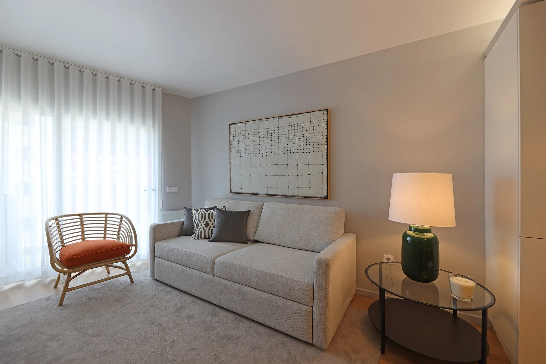 Living room with a light-colored sofa and a floor-to-ceiling curtained window.