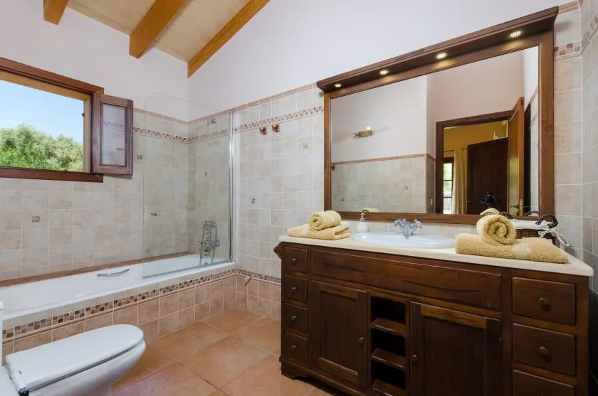 A tiled bathroom with a bathtub, toilet, and wooden vanity beneath a large mirror.