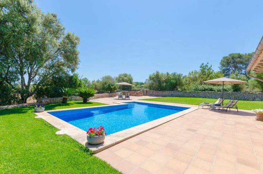 An outdoor swimming pool beside a tiled patio, with green lawn and umbrellas.