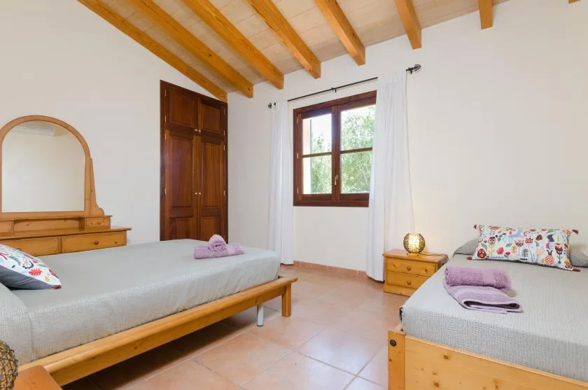 A bedroom with two beds, wooden furnishings, and a window with white curtains.