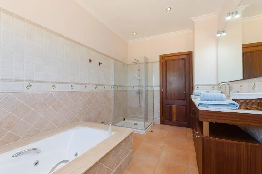 A tiled bathroom with a bathtub, glass shower, and wooden vanity.