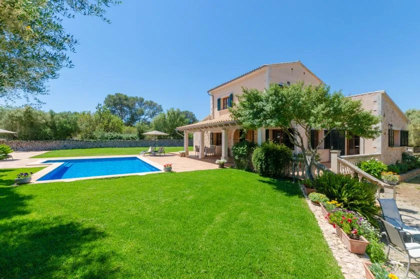 A landscaped yard with a swimming pool beside a two-story house.