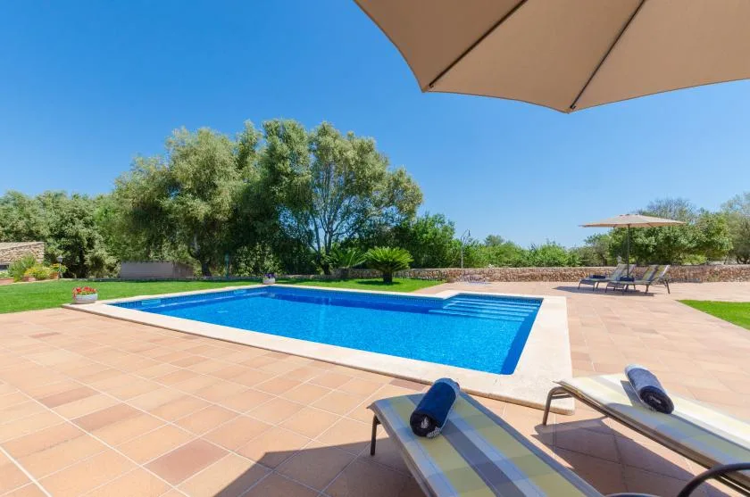 An outdoor swimming pool is surrounded by a tiled patio and lounge seating.