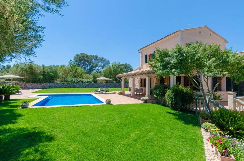 A house and swimming pool overlook a bright green lawn and landscaped garden.