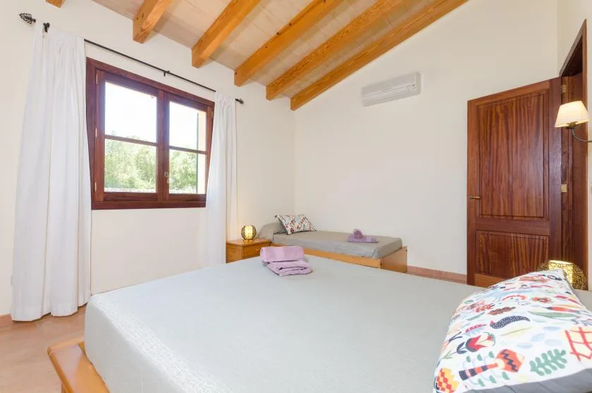 A bedroom with a large bed, a window, and exposed wooden ceiling beams.