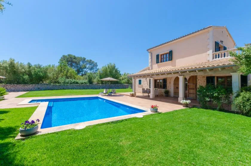A house and patio overlook a swimming pool surrounded by lawn and trees.