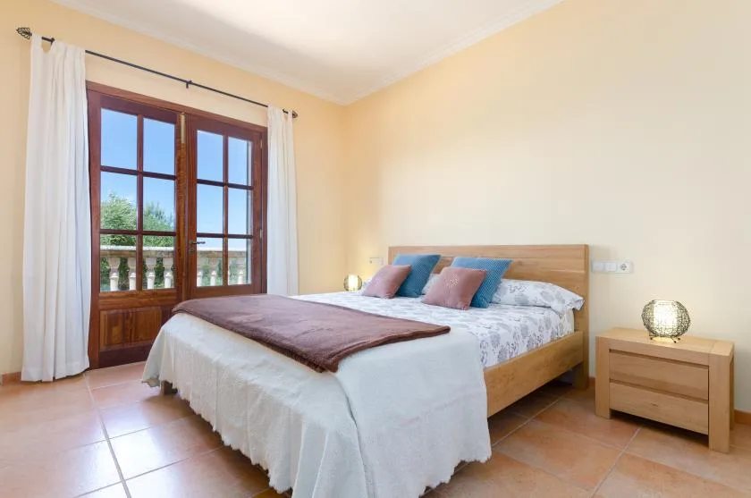 A bedroom with a double bed beside a window with white curtains.