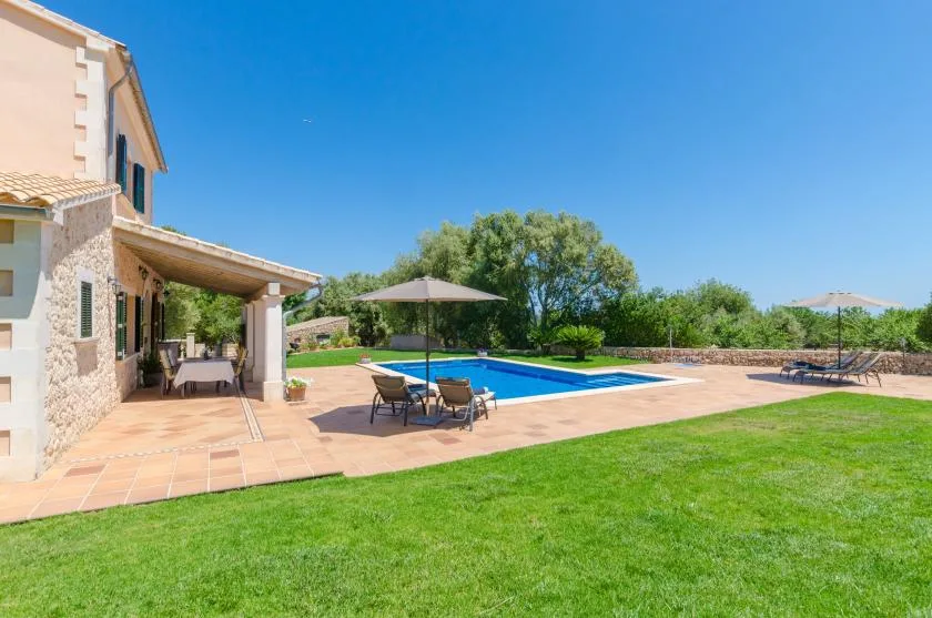 An outdoor pool beside a house, with patio seating and a broad lawn.