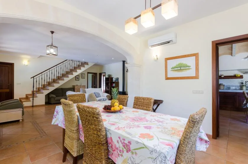 A dining area with a floral tablecloth sits beside an open kitchen and staircase.