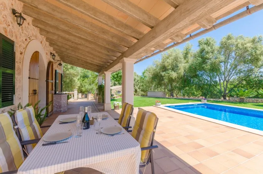 A covered outdoor dining area overlooks a swimming pool and garden.