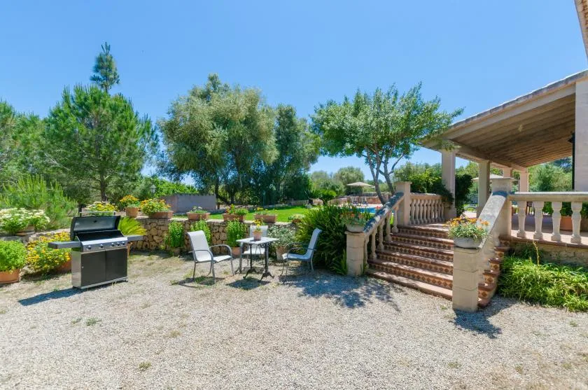 A garden patio with outdoor seating, a grill, and steps to a covered terrace.