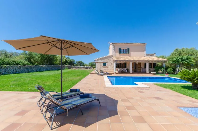 A sunny outdoor pool area with lounge seating and a large patio umbrella.