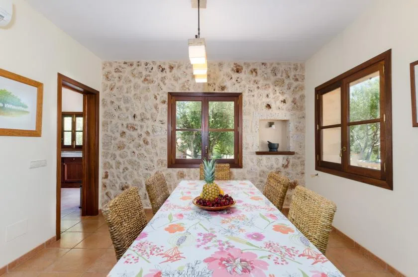 A dining room with a floral tablecloth and windows overlooking greenery.