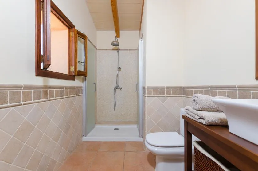 A tiled bathroom with a shower, toilet, and towels on a wooden counter.