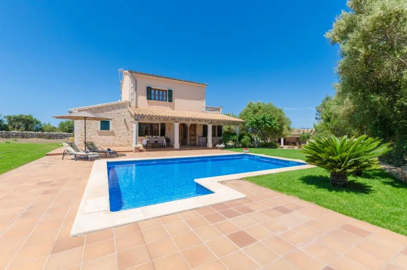 A house and swimming pool sit beside a tiled patio and green lawn.