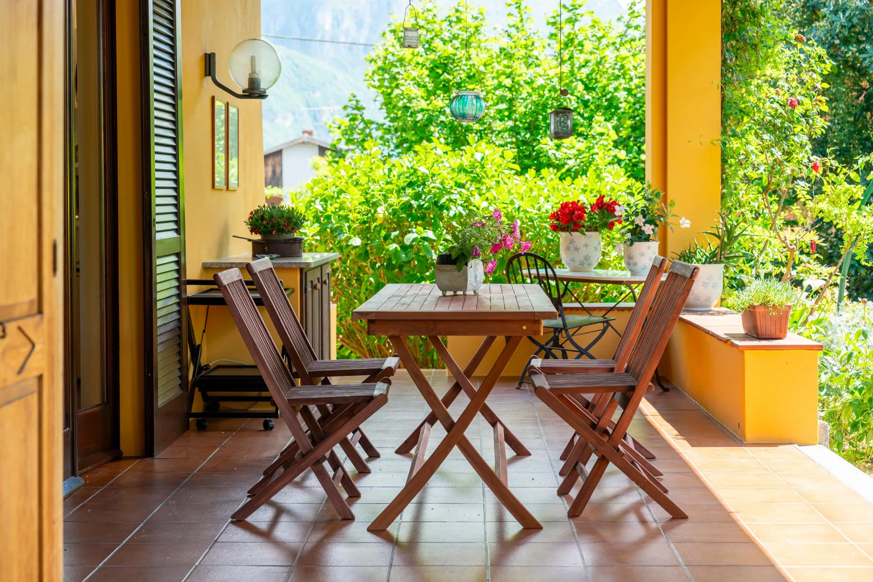 An outdoor dining area with a wooden table and chairs surrounded by plants.
