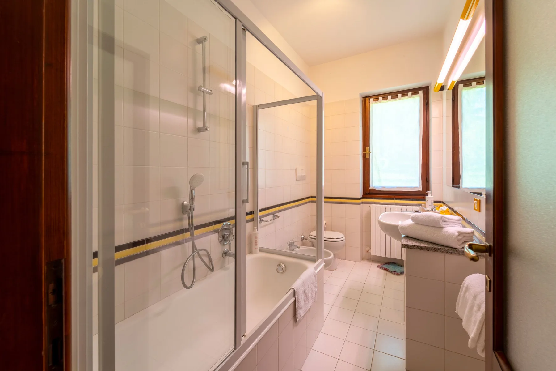 A bright bathroom with a glass shower, bathtub, and vanity.