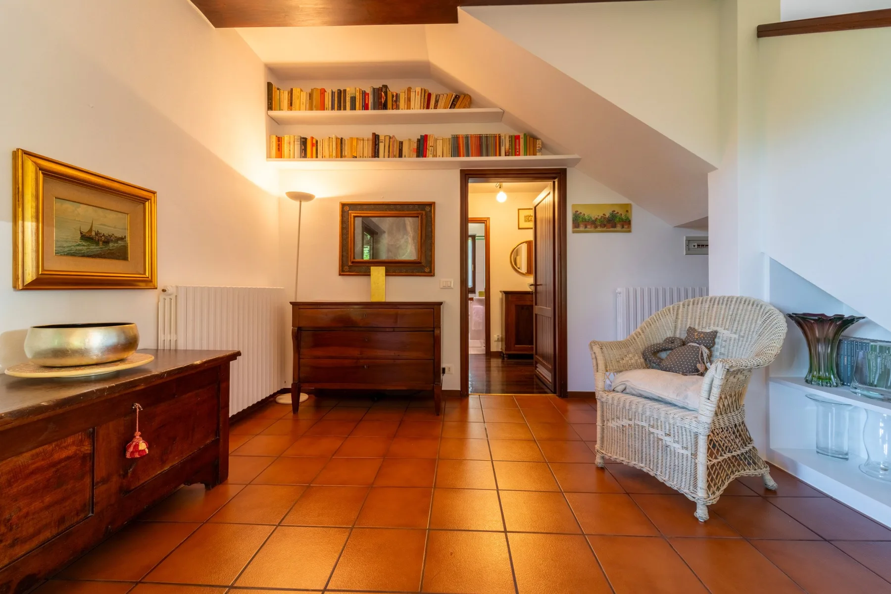A furnished room with bookshelves, wooden furniture, and a wicker armchair.
