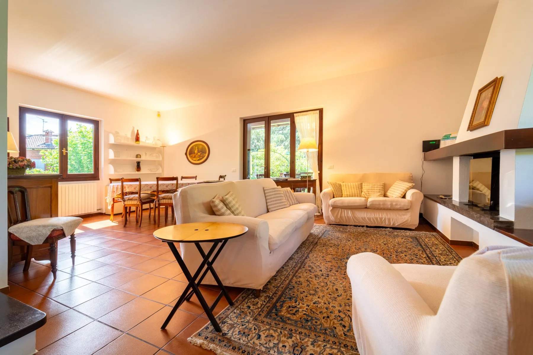 A bright living room with seating around a patterned rug and a fireplace.
