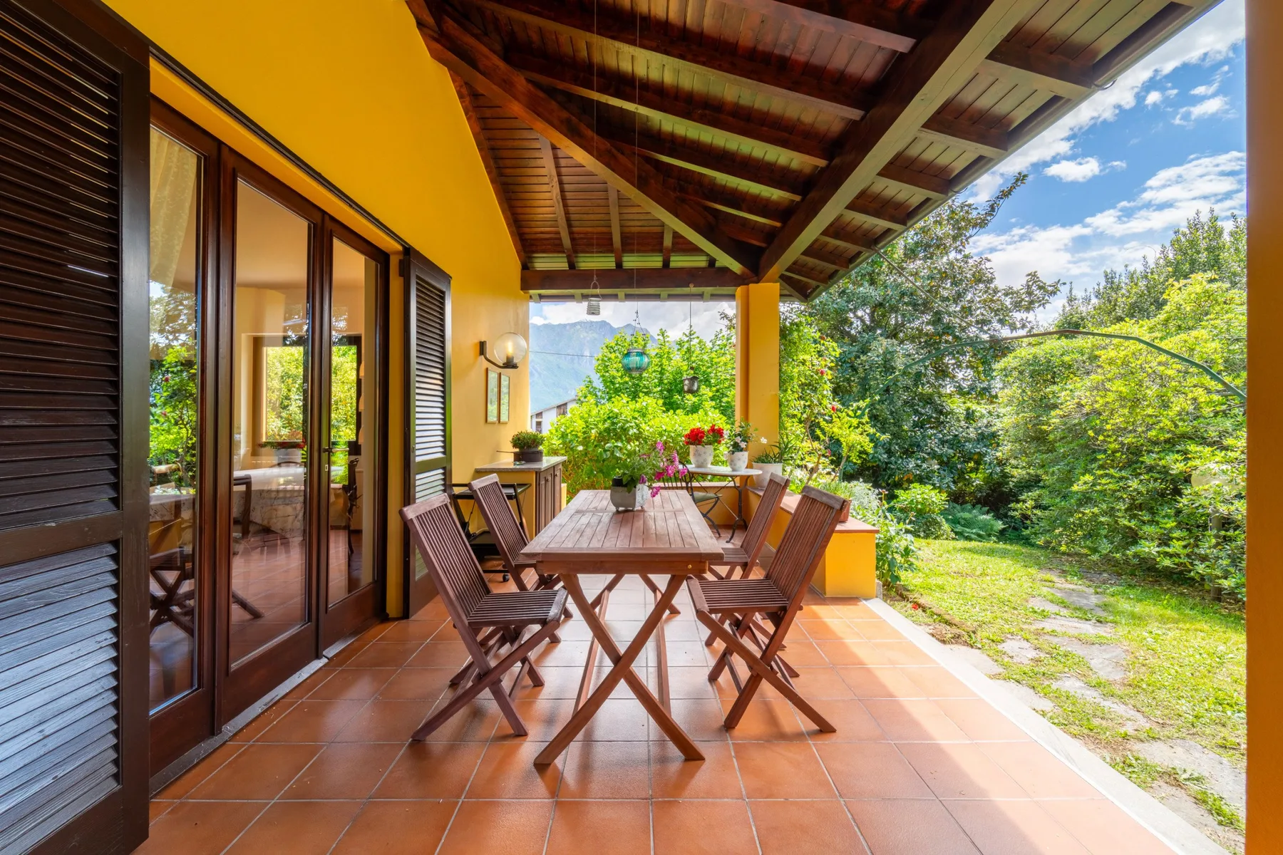 A covered outdoor dining area with a wooden table and surrounding greenery.