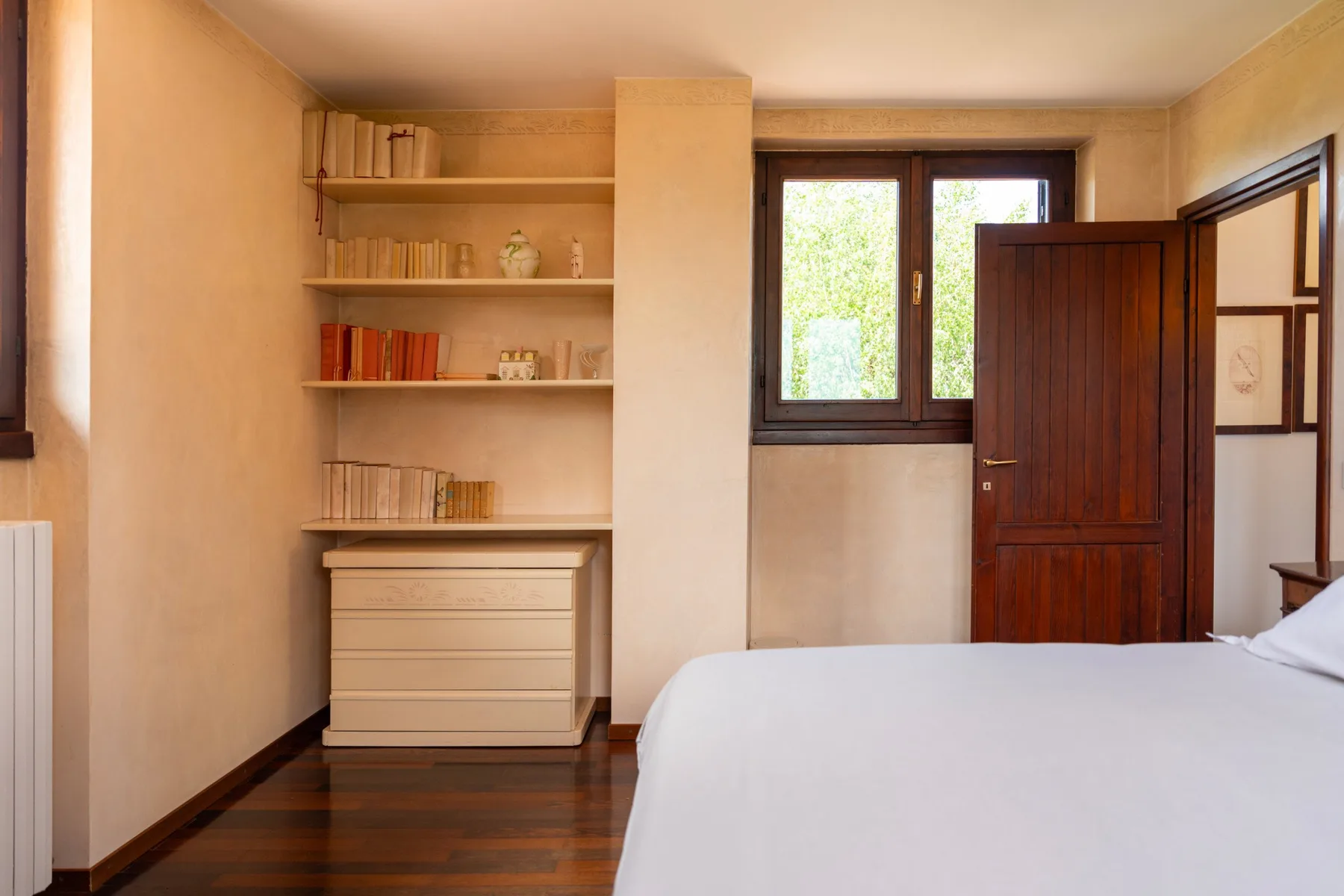 A bedroom with built-in shelves, a dresser, and a bed beside a window.