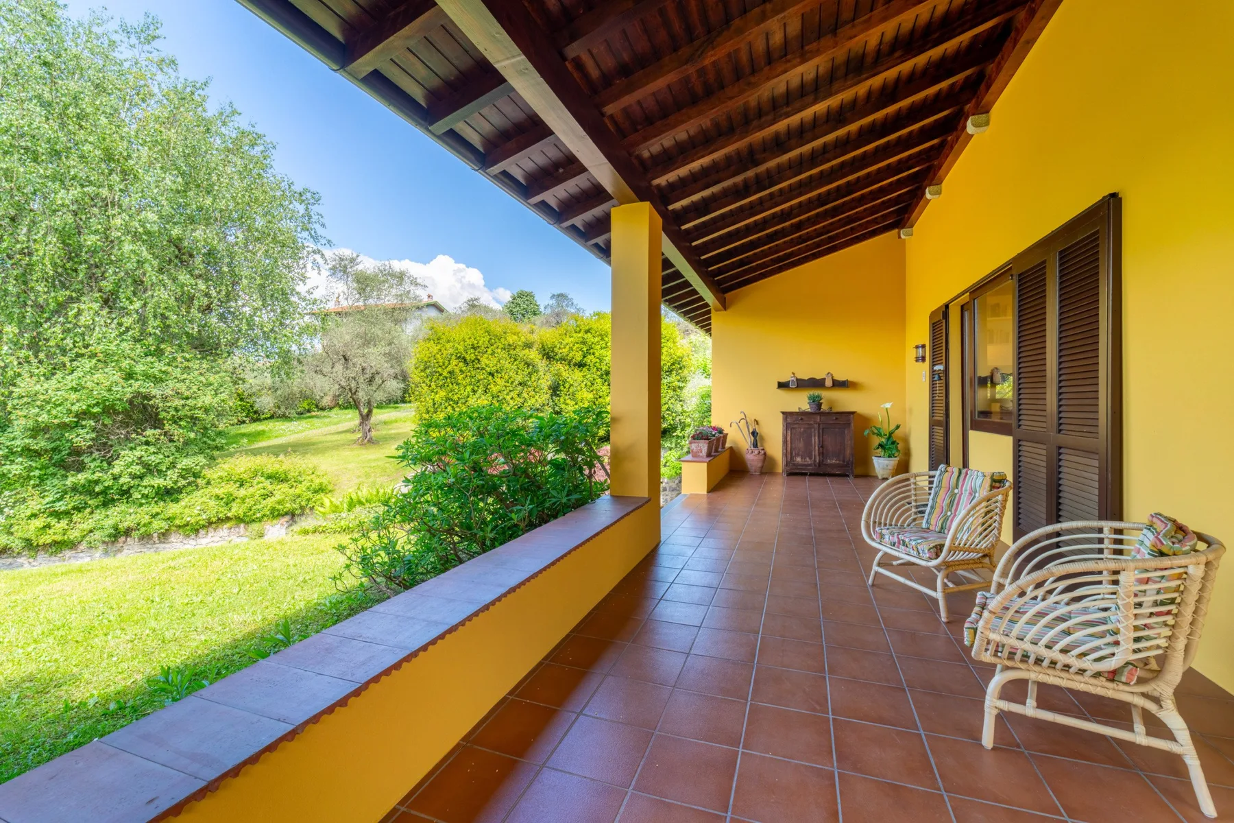 A covered terrace with tiled flooring, seating, and a garden view.