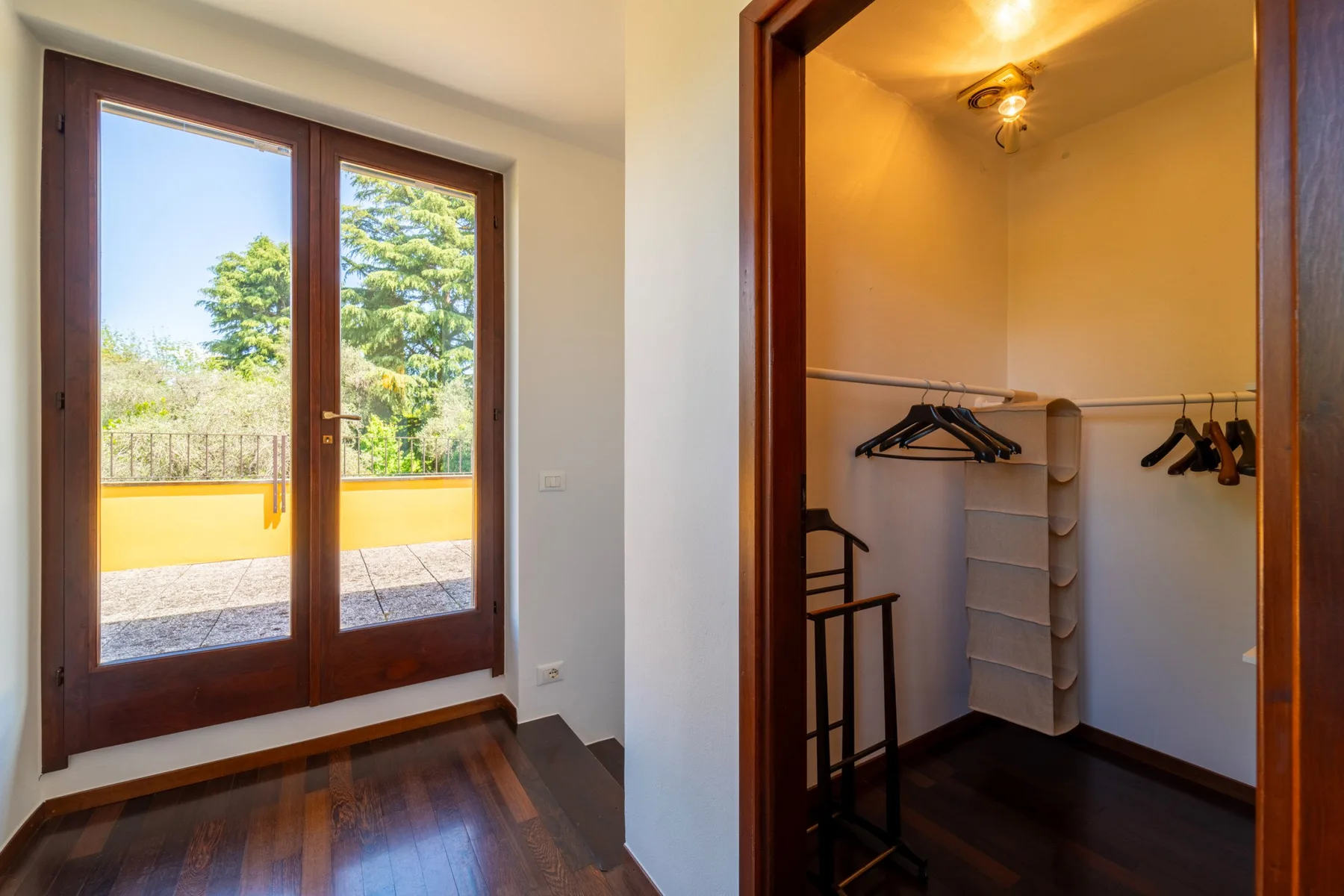 A room with glass doors opening onto a balcony beside a clothes storage area.