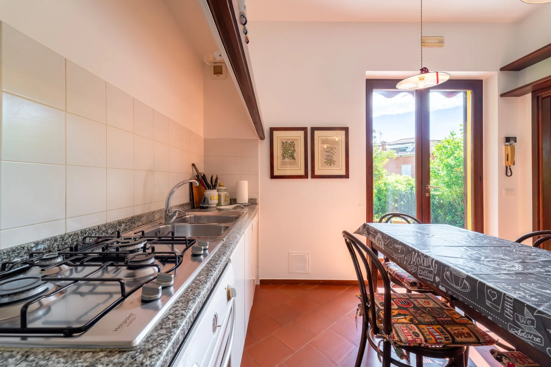 A kitchen with a cooktop, counter, and dining table beside a tall window.