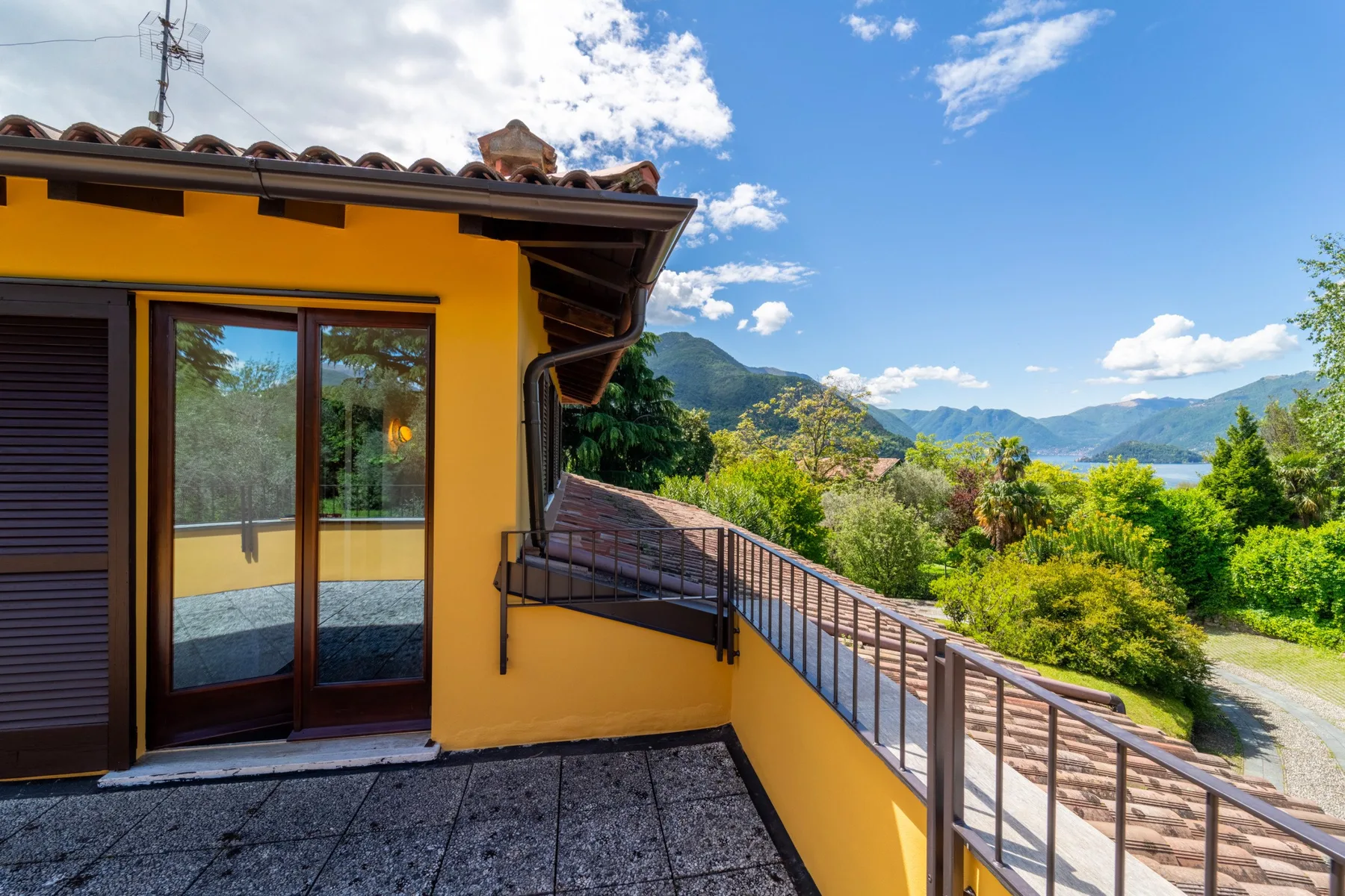 A balcony with a metal railing overlooks green hills beneath a blue sky.