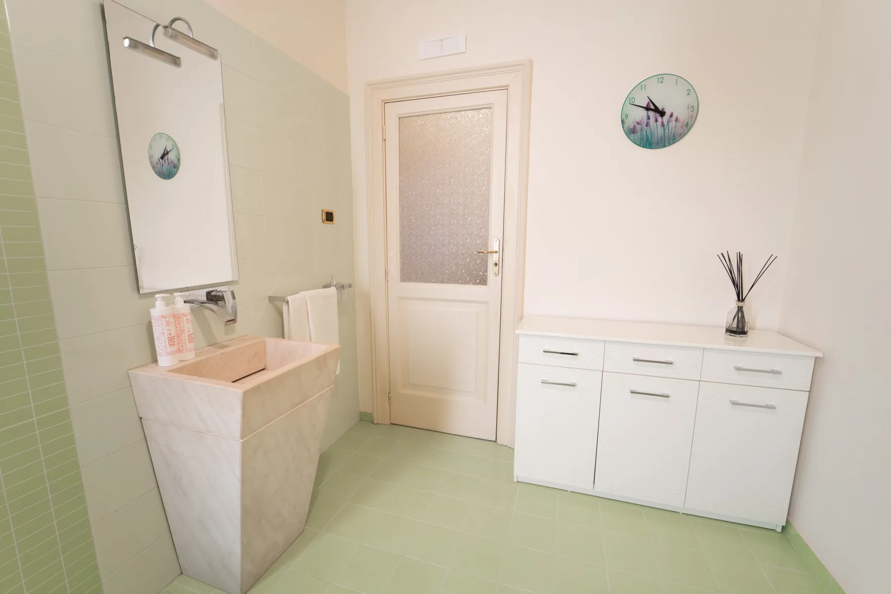 A bright bathroom with a sink, wall mirror, and white storage cabinets.