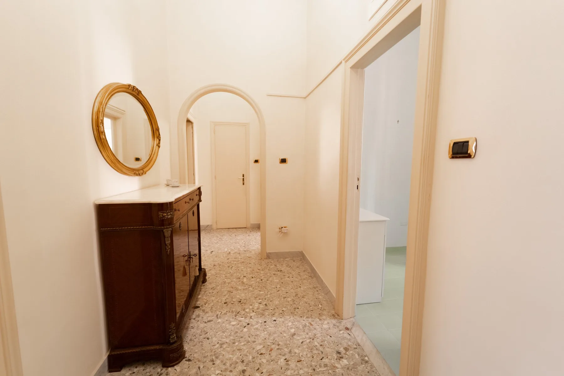 A bright hallway with a dark wooden cabinet and an arched doorway.