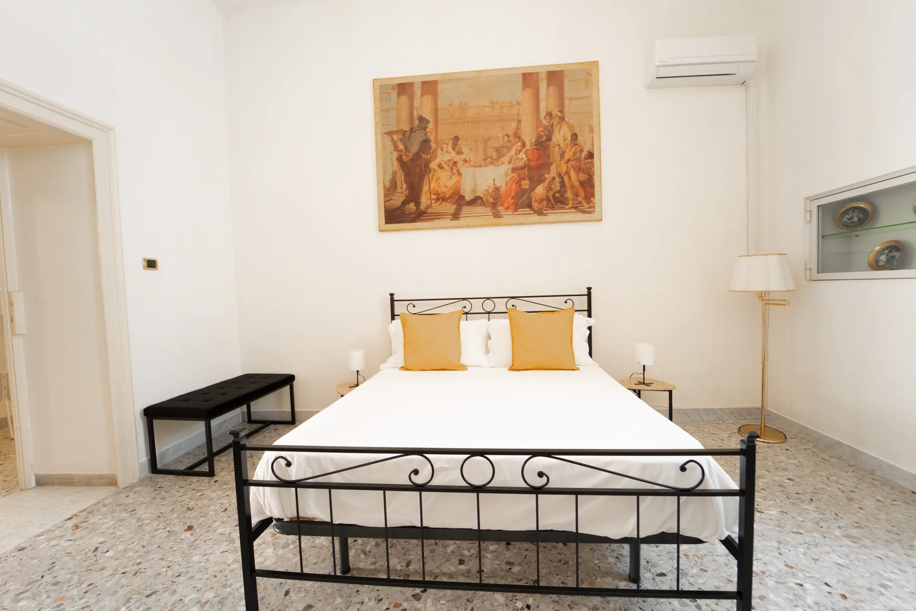 A bedroom with a metal bed, white bedding, and framed artwork above it.