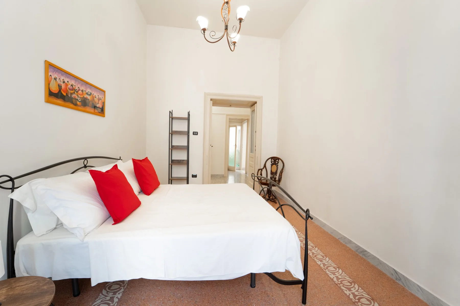 A bright bedroom with a white bed and red accent pillows.