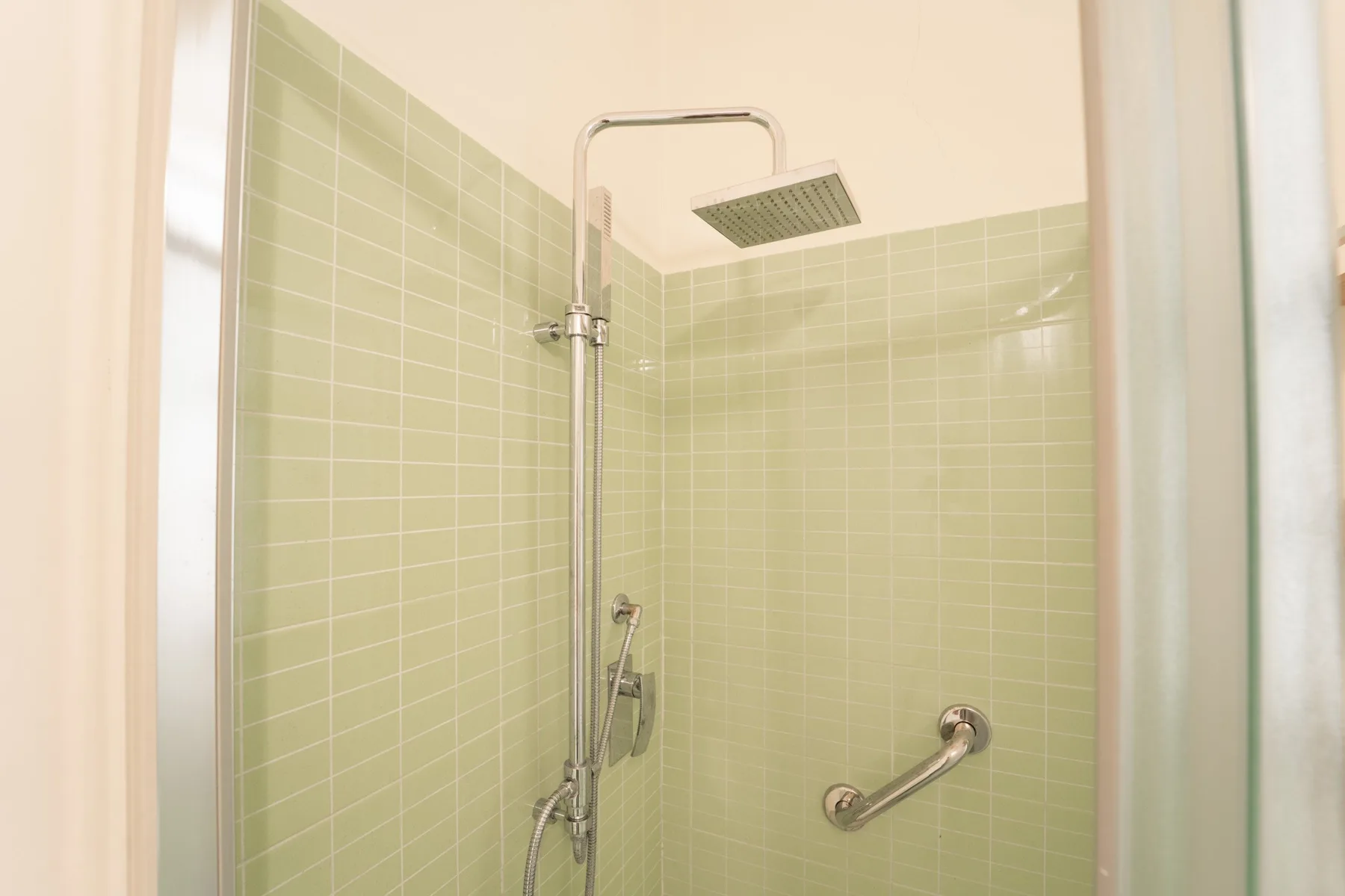 A tiled shower area with a handheld showerhead and wall-mounted grab bar.