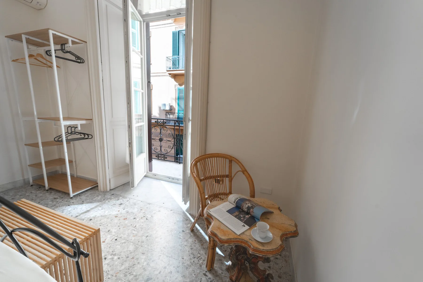 A bright room opens onto a balcony, with a wicker chair and small table.