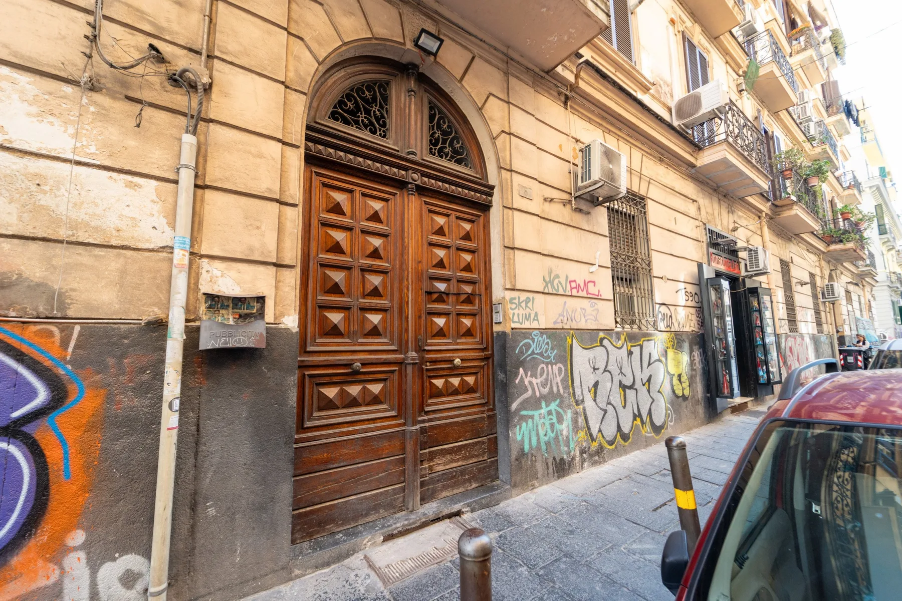 An ornate wooden entrance on a city street with graffiti along the wall.