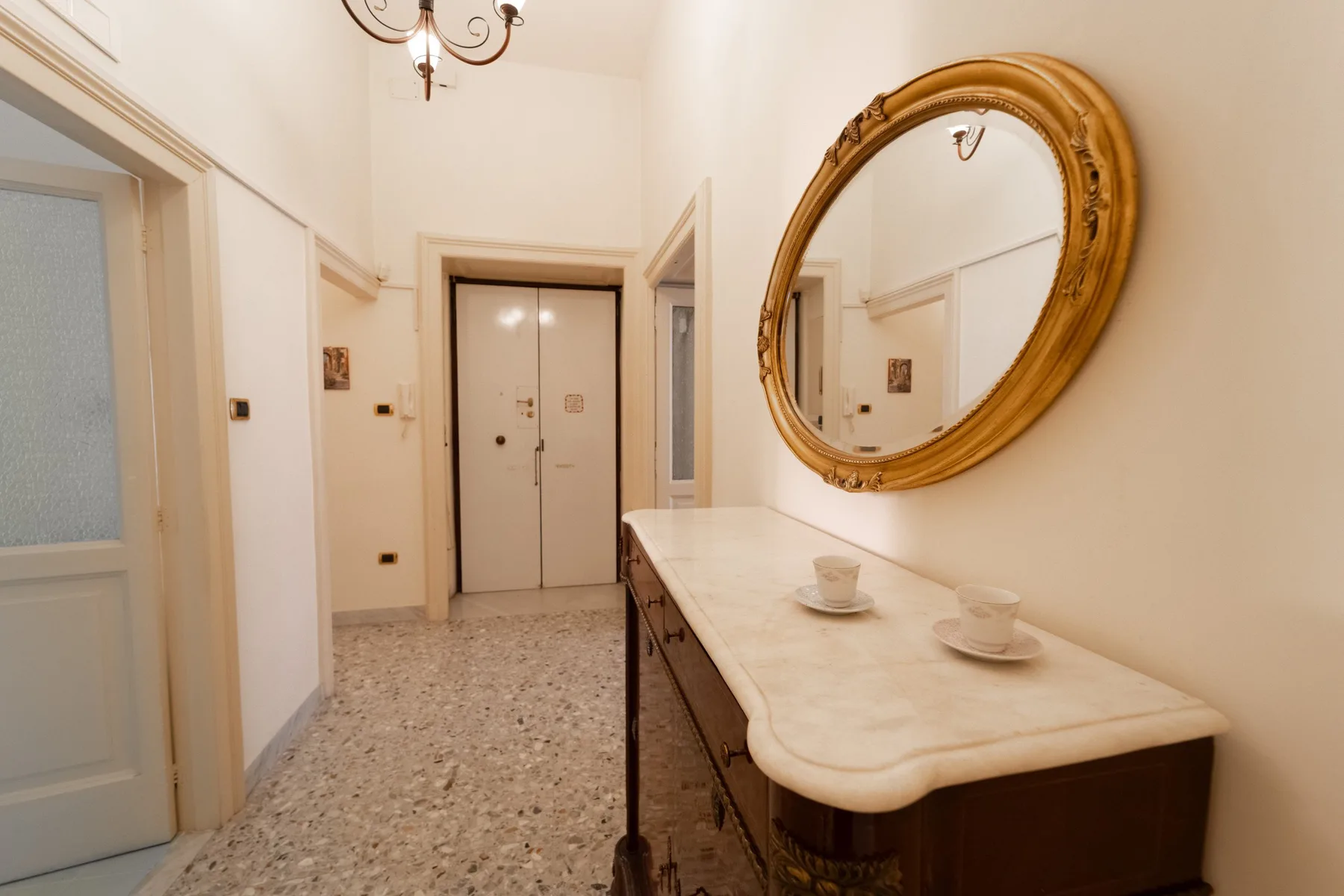 An interior hallway with a long console table and a large oval mirror.
