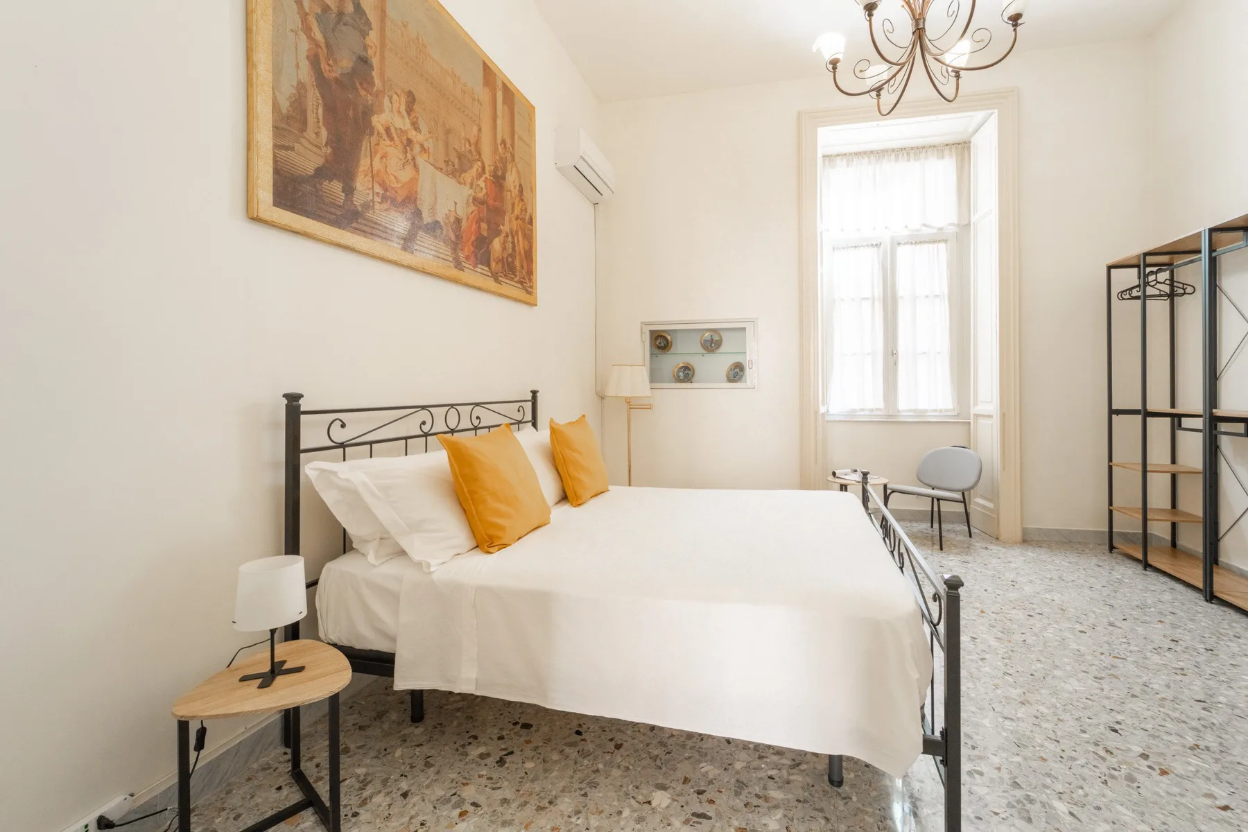 A bright bedroom with a metal bed, white linens, and a tall window.
