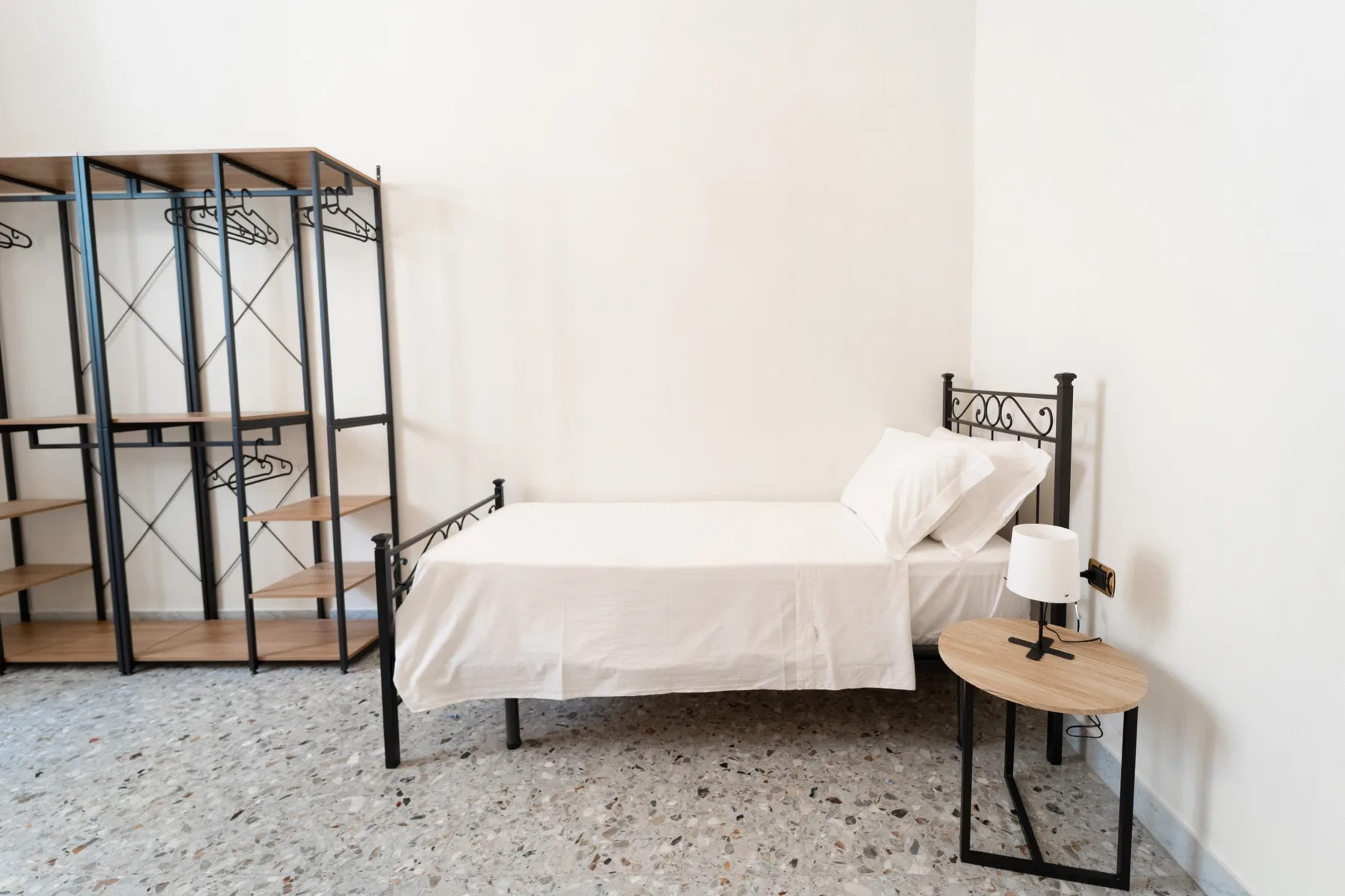 A bright bedroom with a bed, open clothes rack, and bedside table.