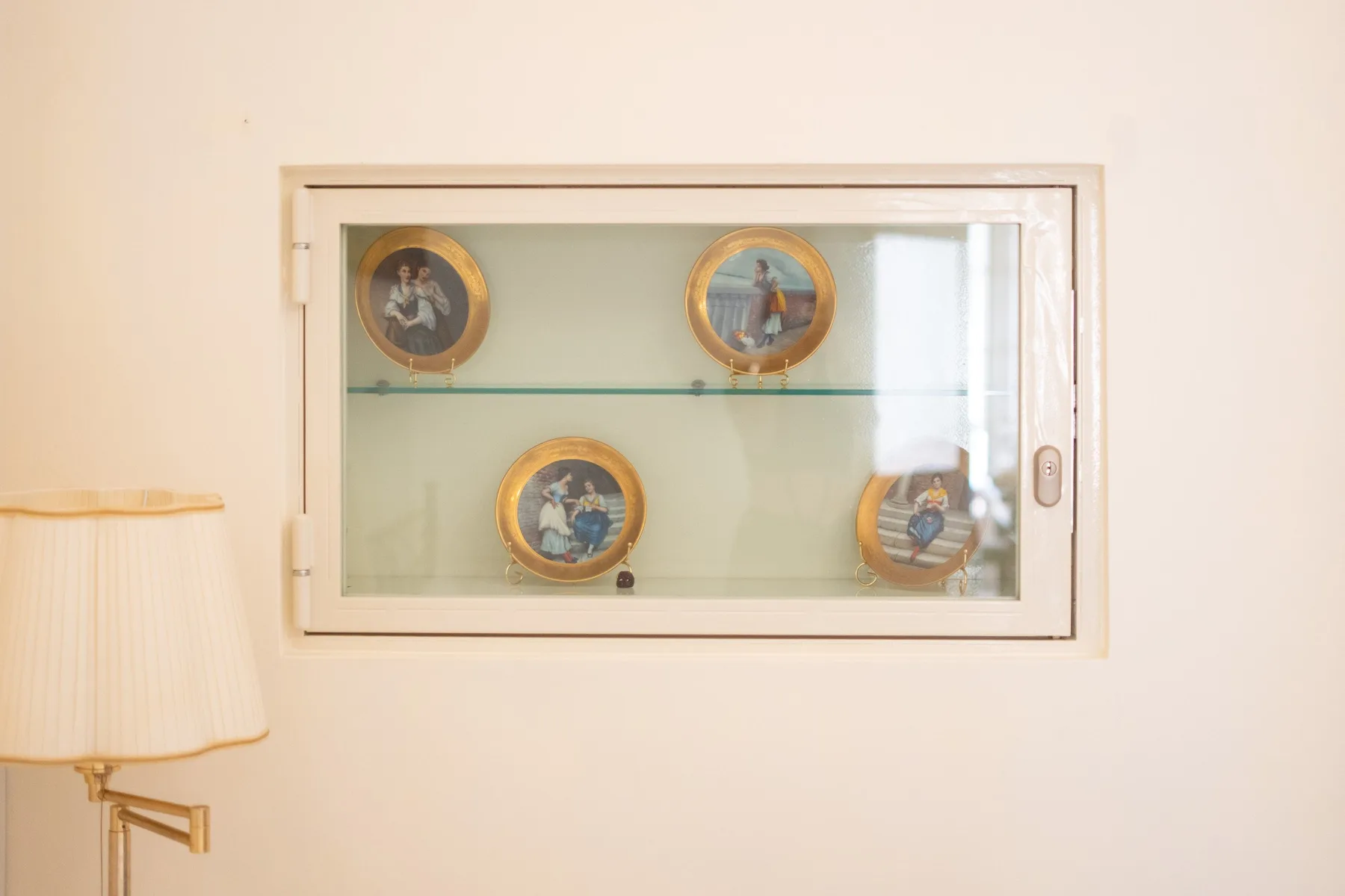 A wall display case holds several decorative plates beside a lamp.