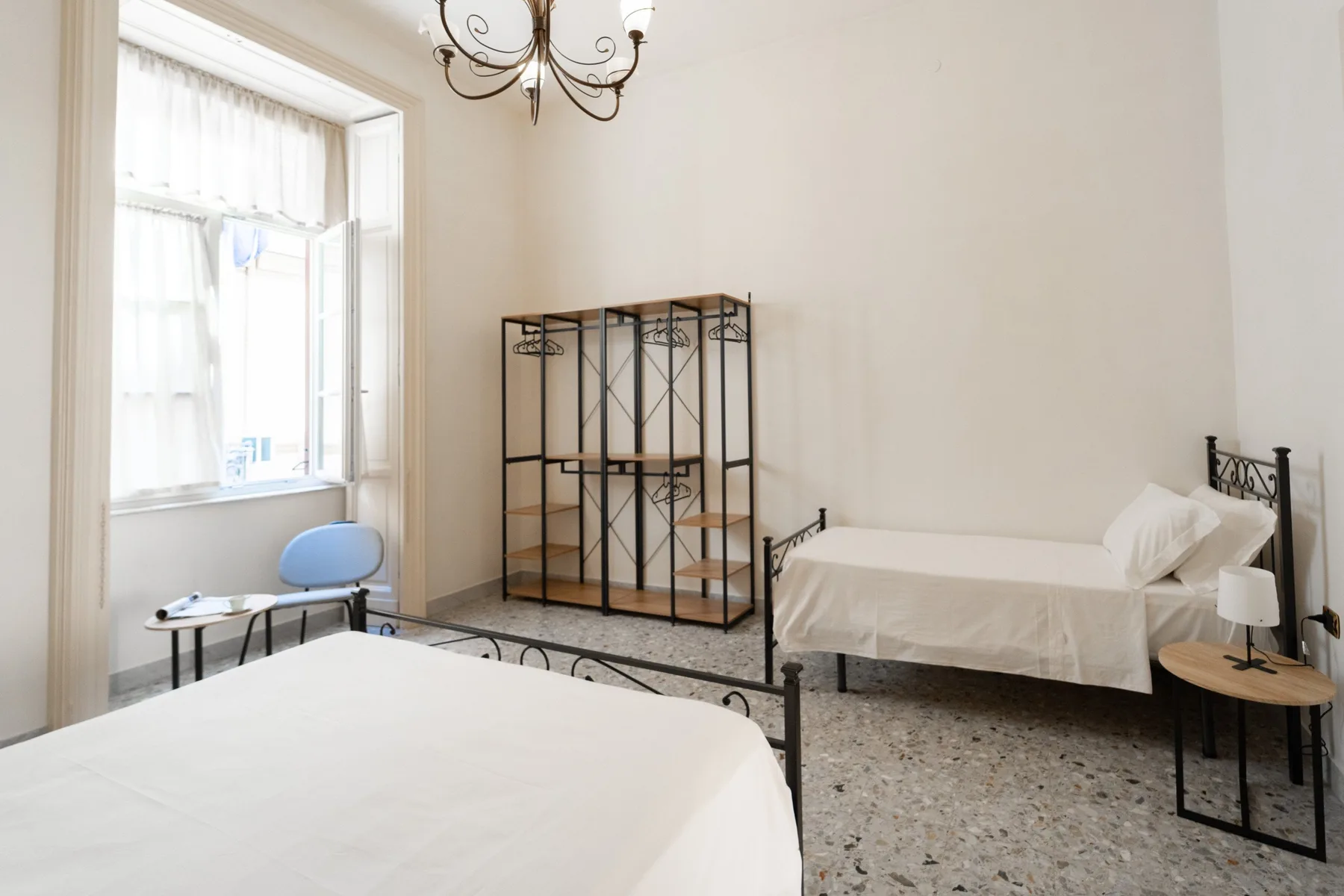 A bright bedroom with two beds, a window, and a freestanding clothes rack.