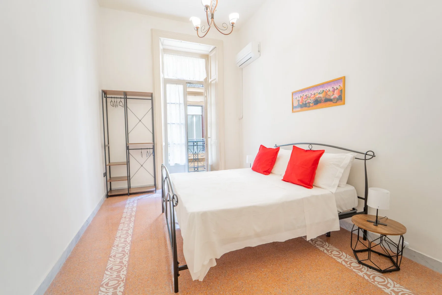 A bright bedroom with a bed dressed in white and red pillows.